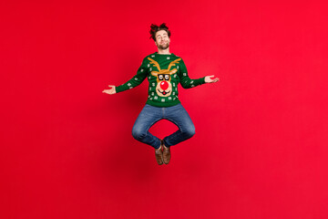 Fototapeta na wymiar Full size photo of good mood smiling guy jumping wear green sweater reindeer print isolated on red color background