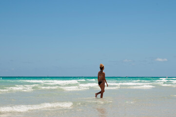 Fototapeta na wymiar A woman with a fit body, wearing bikini walking on Miami beach on a summer day with a cloudless sky