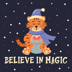 Tiger in santa hat and scarf is sitting with a gift.  Believe in magic lettering.  Winter greeting card.