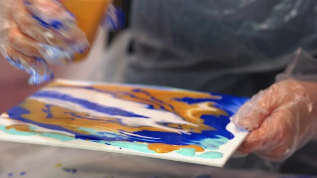 Artist pouring acrylic paints onto the canvas.