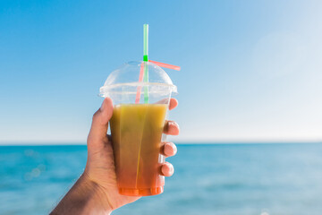 The guy's hand holds a colored chilled non-alcoholic cocktail against the background of the sea