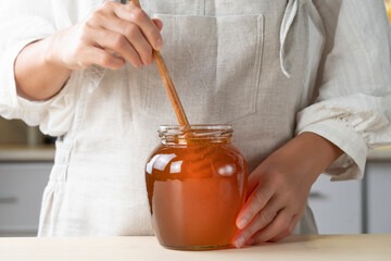 farmer pours a fresh harvest of honey into a glass jar. Organic Honey dripping, pouring from honey dipper in glasses bowl. Close-up 