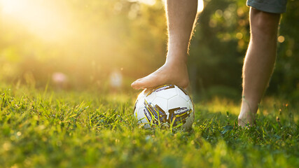 Male foot without shoes on a soccer ball on a grassy field with a sun glare and a copy space.