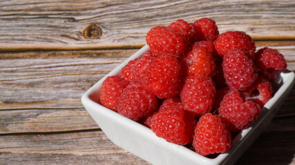 a white bowl with ripe raspberries on a wooden surface summer is sunny