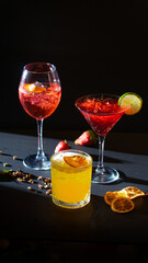 Aperol Spritz and red and yellow aperitif cocktails in glass with ice on black background
