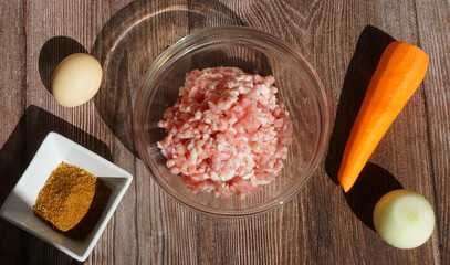 ingredients for making minced meat - meat, carrots, onions, chicken egg, spices on a wooden board, a glass bowl with minced meat - on a wooden table, summer, sunny