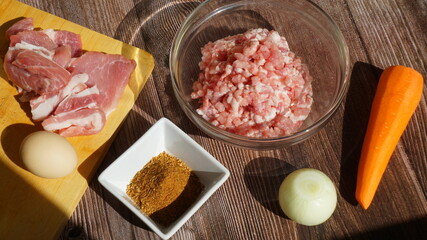ingredients for making minced meat - meat, carrots, onions, chicken egg, spices on a wooden board, a glass bowl with minced meat - on a wooden table, summer, sunny