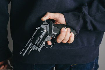 Man holding gun behind his back on grey background, closeup - obrazy, fototapety, plakaty