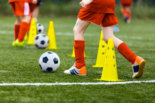 Closeup image of football players running balls between training cones on practice unit. Young boys on football camp. School soccer players improving dribbling skills
