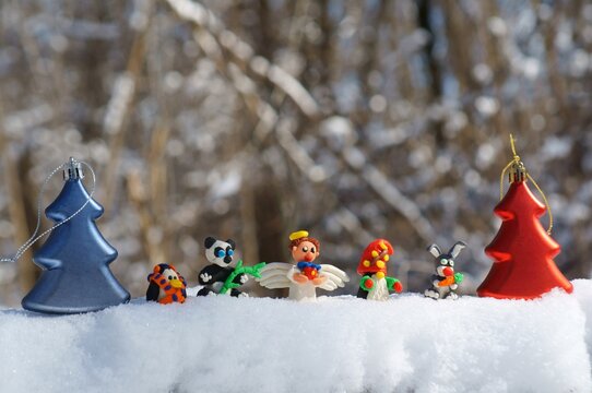 Figurines of fairy-tale characters in the winter forest. An angel with a gift, a dwarf, a rabbit with a carrot, a panda, a penguin in a scarf. There are toy Christmas trees nearby.