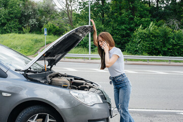 A young girl stands near a broken-down car in the middle of the highway and calls for help on the...