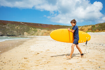 Boy walk on beach into sea hold surfboard in hands