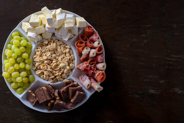 assorted appetizer on a plate shot from above. nuts, bacon, cheese, chocolate, grapes on a wooden background