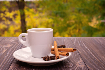 Cup of coffee with red leaves on a wooden surface with a forest in the background