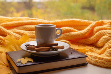 White scarf, cup of coffee with scattered coffee beans, dry yellow leaves on a wooden table. Autumn mood, copy space.