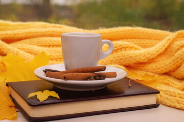 White scarf, cup of coffee with scattered coffee beans, dry yellow leaves on a wooden table. Autumn mood, copy space.