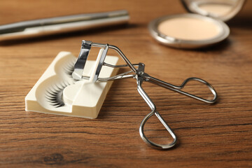 False eyelashes and curler on wooden table, closeup