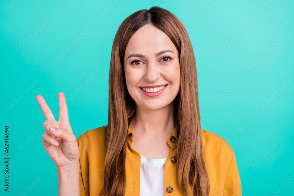 Sticker Photo of funky shiny young woman dressed yellow shirt smiling showing v-sign isolated teal color background