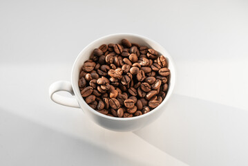 A white cup filled with brown coffee beans on white background
