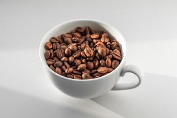 A white cup filled with brown coffee beans on white background