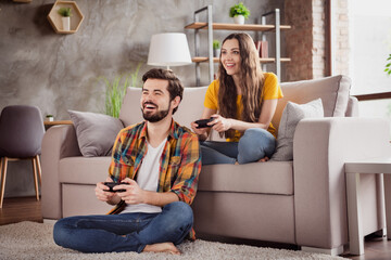 Photo of funny funky young couple wear casual outfits smiling sitting couch holding playstation gamepads indoors house room
