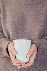 Woman_in_sweater_holding_white_coffe_cup_in_her_hands