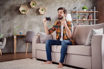 Photo of funny lucky young lovers dressed casual clothes sitting sofa smiling rising fist holding playstation gamepad indoors loft apartment