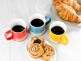three mugs of black coffee, three pastries on a plate and two coissants