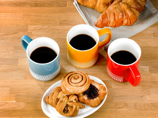 three mugs of black coffee, three pastries on a plate and two coissants