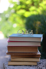 Stack of vintage hardcover books and reading glasses in a garden. Selective focus.