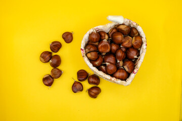 Heart-shaped wicker basket full of chestnuts with yellow background