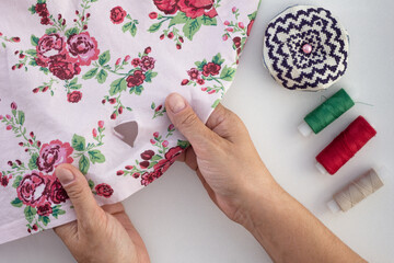 Woman hand holding torn cloth showing hole on the white background with needle bar and thread