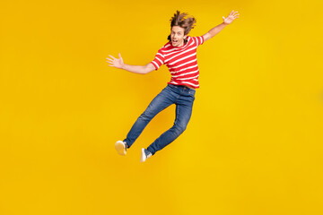 Fototapeta na wymiar Photo of funny excited young man wear striped t-shirt smiling jumping high isolated yellow color background