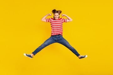 Fototapeta na wymiar Photo of charming strong young guy dressed red t-shirt jumping high showing muscles smiling isolated yellow color background