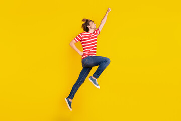 Fototapeta na wymiar Photo of cute strong young man wear striped t-shirt jumping high looking empty space isolated yellow color background