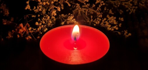 A red candle burns in the dark. A lit candle.