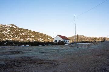 Casa blanca rodeada de montañas nevadas en el amanecer sobre un cielo azul.