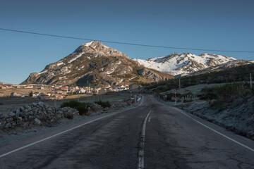 Carretera de un pueblo rodeado de montañas nevadas en el amanecer sobre el cielo azul.