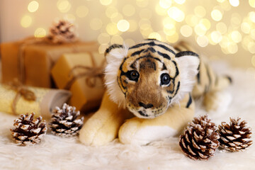 A toy tiger among gifts and pine cones against a background of festive bokeh. New Year, Eastern calendar, Year of the Tiger.