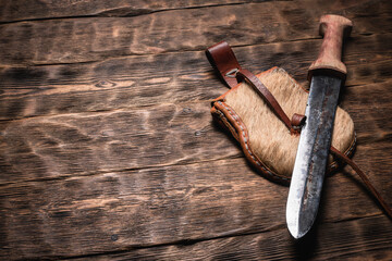 Ancient sword and leather wallet on the wooden table background with copy space.