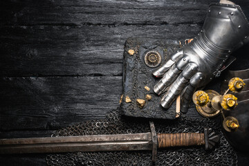 Knight sword and ancient book on the black wooden flat lay table background with copy space.