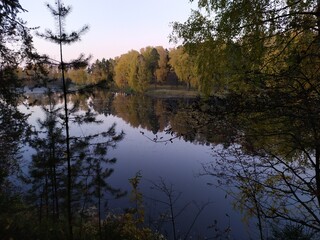 Fall landscape with reflection of trees in the calm river water in sunny autumn evening