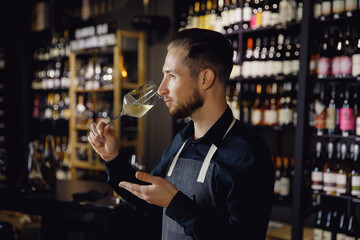 Sommelier man holds glass with white wine in restaurant, tests aroma and color