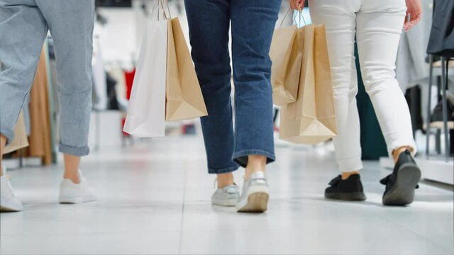 Female legs in jeans of different color walking in mall in slow motion. Following shot of women carrying shopping bags. Friends spending time together. Concept of shopping