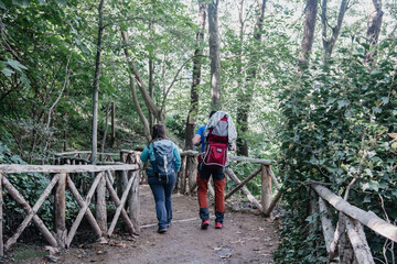 Una pareja de excursionistas haciendo senderismo por un camino mientras portan un bebé a cuestas...