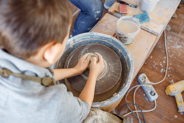 Child working on pottery wheel. Kids arts and crafts class in workshop. Little girl creating cup and bowl of clay. Creative activity in school.