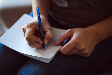 Close up shot of female's hand writing down the note on empty notepad book in her lap
