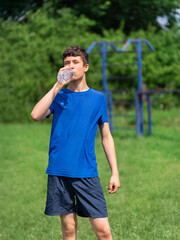 Fototapeta na wymiar teenage boy exercising outdoors, sports ground in the yard, he opens a bottle of water and drinks, healthy lifestyle