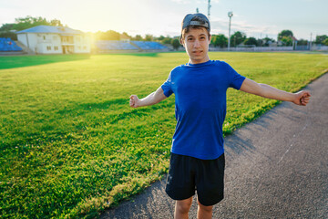 teen boy boy does physical exercises at the stadium track, a soccer field with green grass - concept of sports and health