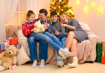 Winter holiday concept - Family sitting on a couch and posing in new year or christmas decoration. Children and parents. Holiday lights and gifts, Christmas tree decorated with toys.